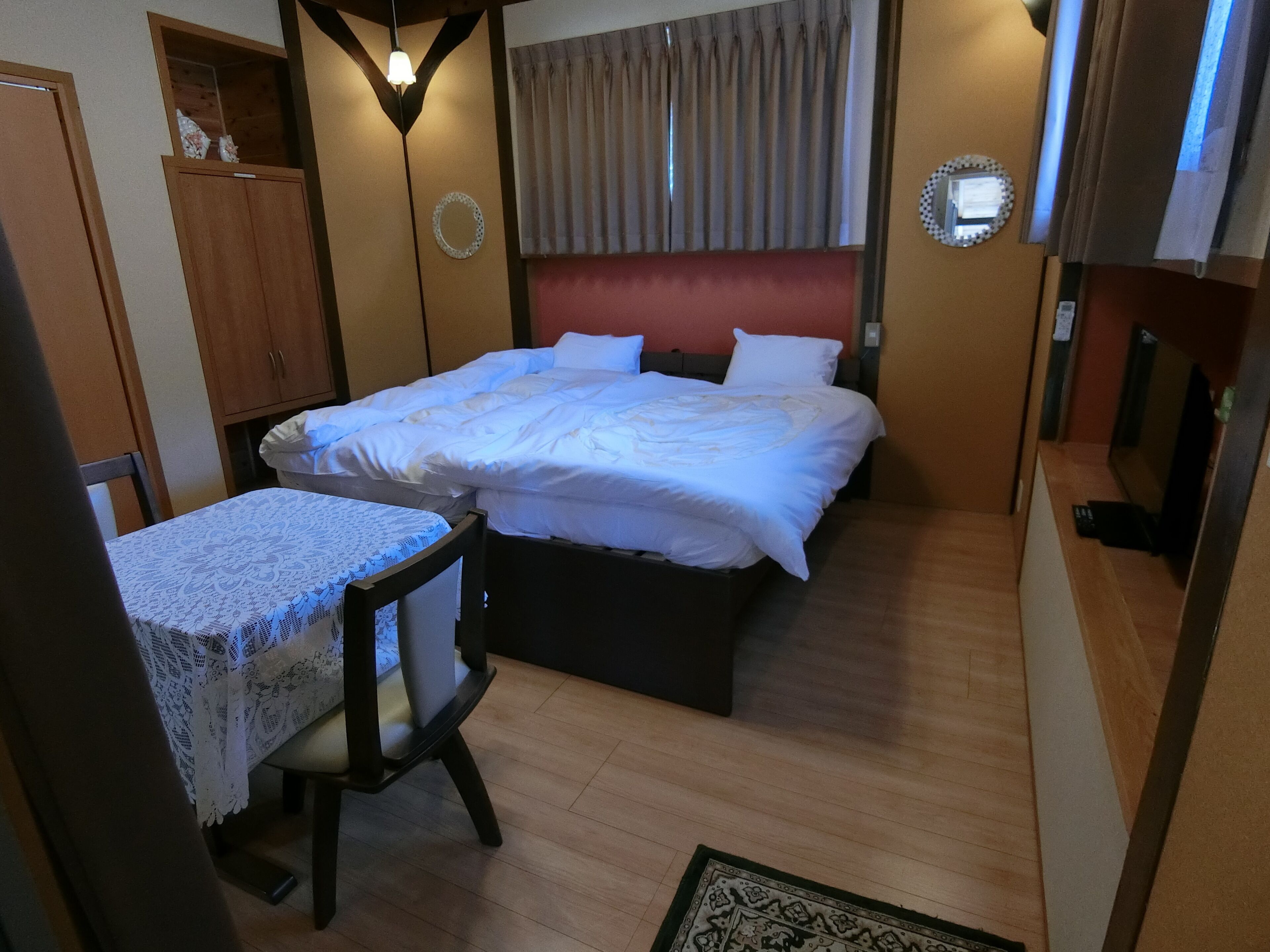 Un dormitorio con cama, escritorio, silla, armario de madera y espejo en la pared.