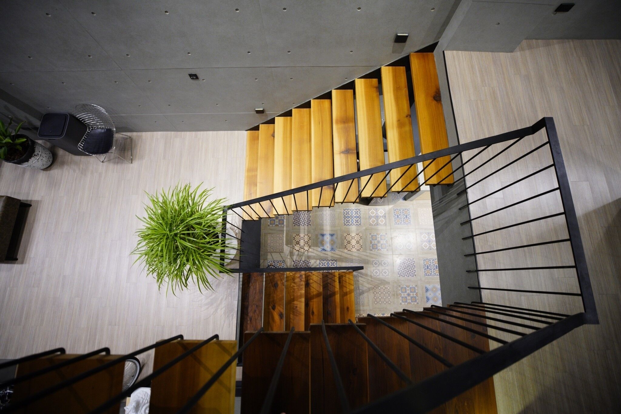 Una escalera moderna con escalones de madera y barandilla metálica, que conduce a un rellano con suelo de baldosas estampadas.