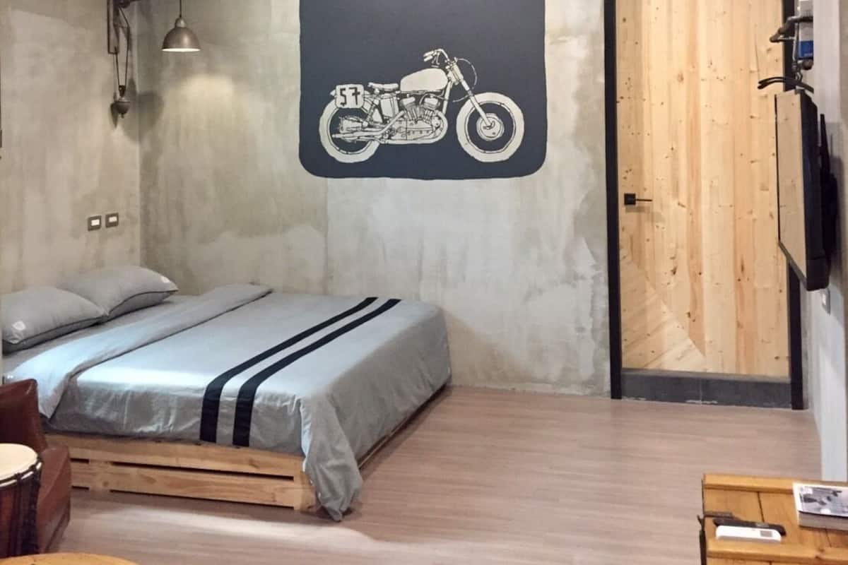 A bedroom with a bed, a motorcycle wall art, a wooden door, and a small wooden table.
