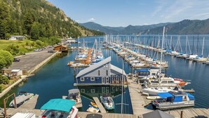 A marina with multiple boats docked, a wooden pier, and a building with a blue roof. - Lakefront Float Home with Huge Deck & Water Toys (Bayview)