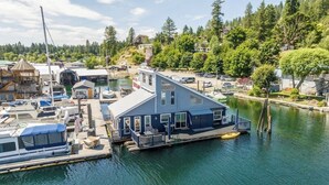 A houseboat docked at a marina with a docked boat, a covered area, and a view of the surrounding trees and hills. - Lakefront Float Home with Huge Deck & Water Toys (Bayview)