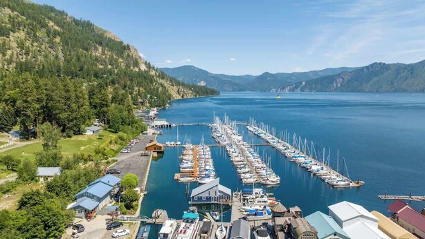 A marina with boats docked, surrounded by forested hills and a clear sky. - Lakefront Float Home with Huge Deck & Water Toys (Bayview)