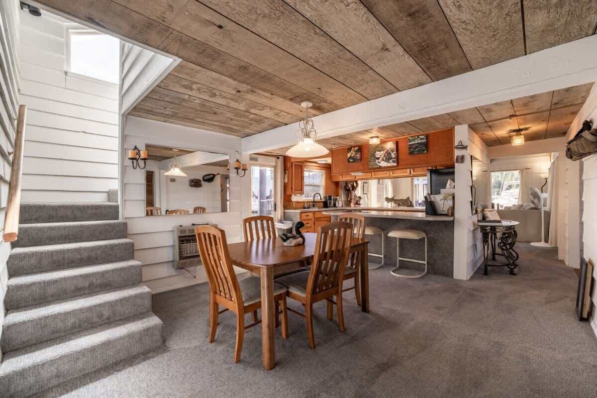Une cuisine spacieuse avec des meubles de rangement en bois, un coin repas comprenant une table et des chaises, et un escalier menant à un autre niveau.