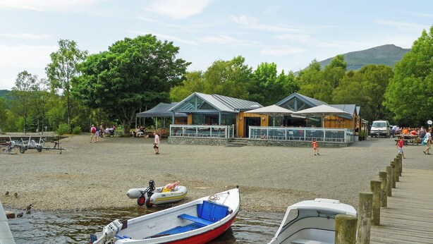 Une zone au bord du lac où sont amarrés des bateaux, avec une jetée en bois et un restaurant doté d’une terrasse.