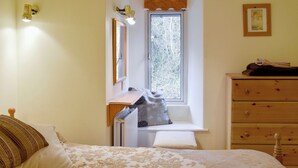 Une chambre à coucher comprenant un lit, une commode, une fenêtre donnant sur des arbres et un luminaire fixé au mur.