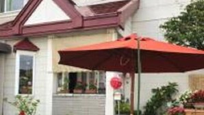Een huis met een rood dak, een tuin vol verschillende planten en een rode parasol.