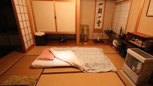 Een traditionele Japanse kamer met tatami vloerbedekking, een futon bed, een verwarming en een shoji schuifdeur.