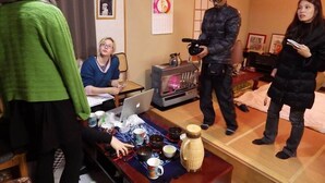 Een kamer met een houten vloer, een tafel met diverse spullen, een laptop en een persoon die een camera gebruikt.