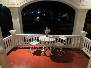 A balcony with white railings, a small round table, two white chairs, and a vase with flowers.