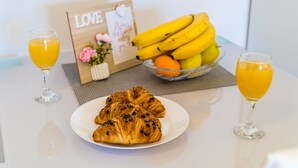 Esmorzar amb croissants, un bol de fruita i dos vasos de suc d'aranja damunt una taula blanca.