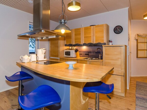 Una cocina compacta con una isla central, armarios de madera, un microondas y un reloj en la pared.