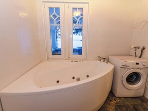 Un baño con una bañera grande, una lavadora y un ventanal con vistas a árboles.