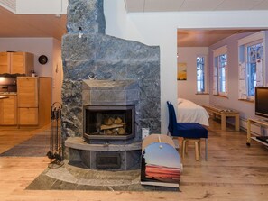 Una sala moderna con chimenea de piedra, piso de madera, comedor y vistas al exterior a través de amplios ventanales.