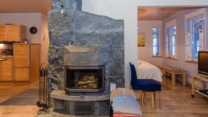 Ein modernes Wohnzimmer mit Kamin aus Stein, Holzmöbeln und Blick ins Freie durch große Fenster.
