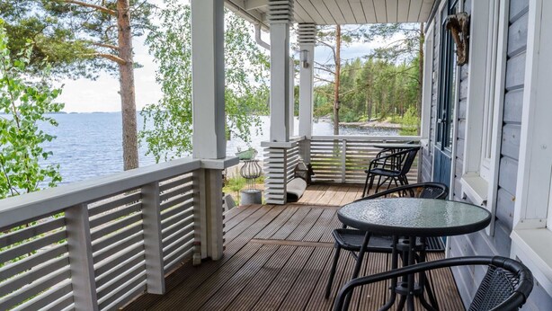 Ein überdachter Balkon mit Blick auf einen See, ausgestattet mit einem Tisch und Stühlen.