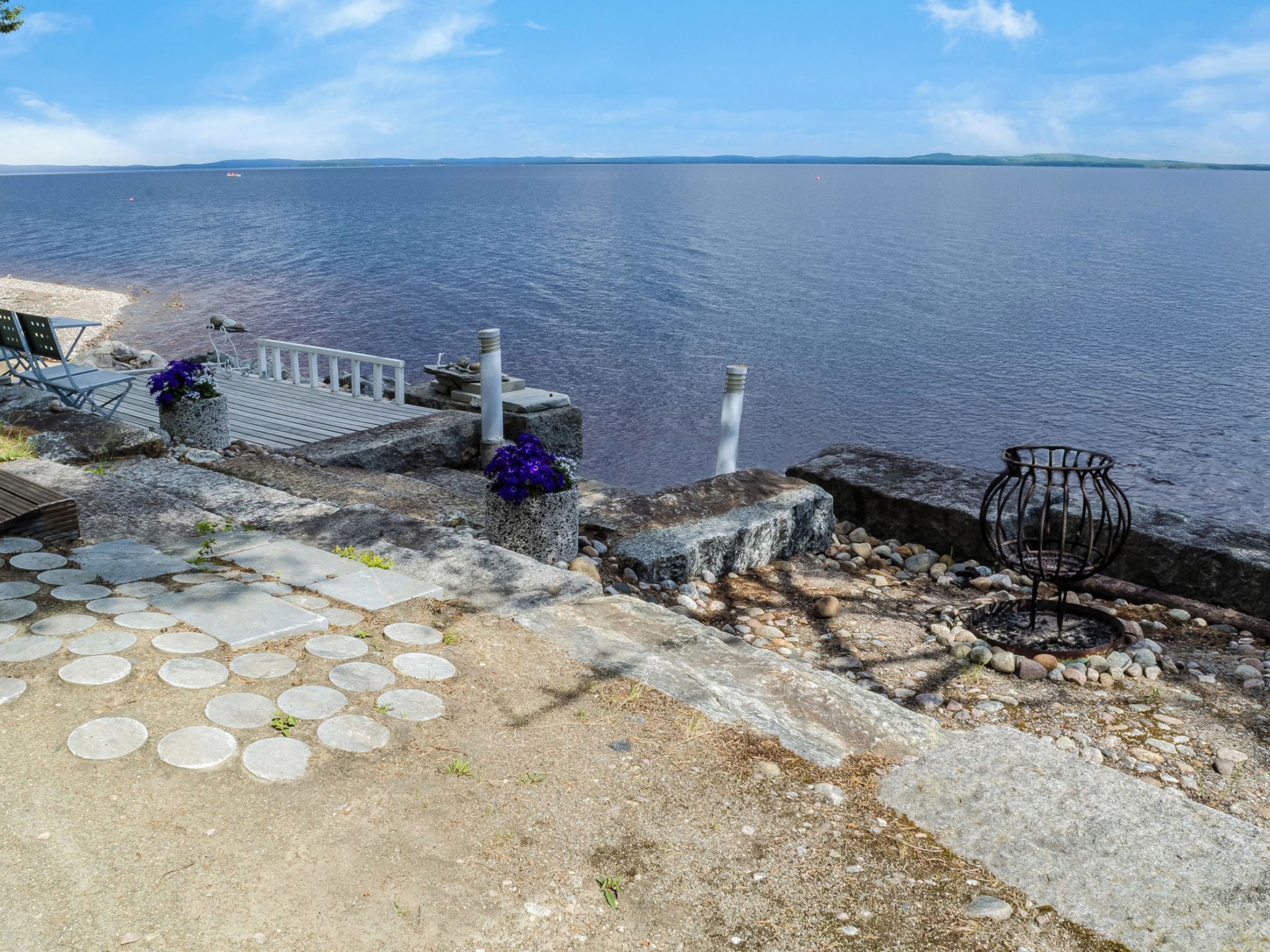 A waterfront property with a stone staircase leading to a dock, a metal chair, and a small garden area with a bird feeder.