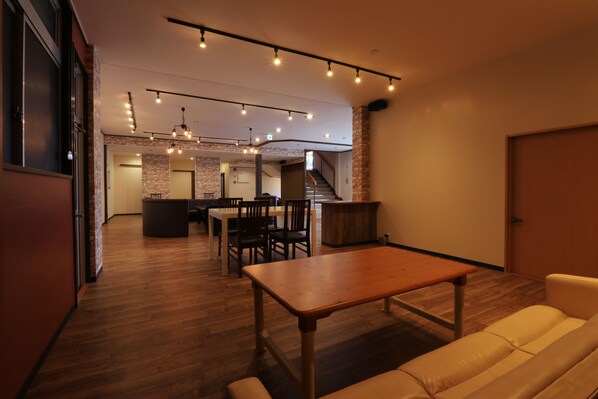 A spacious room with a wooden table and a sofa, a staircase, and a kitchen area in the background.