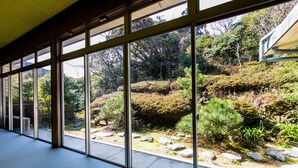 Ein Gebäude mit großen Glasfenstern und Blick auf einen angelegten Garten mit Steinen und Sträuchern.