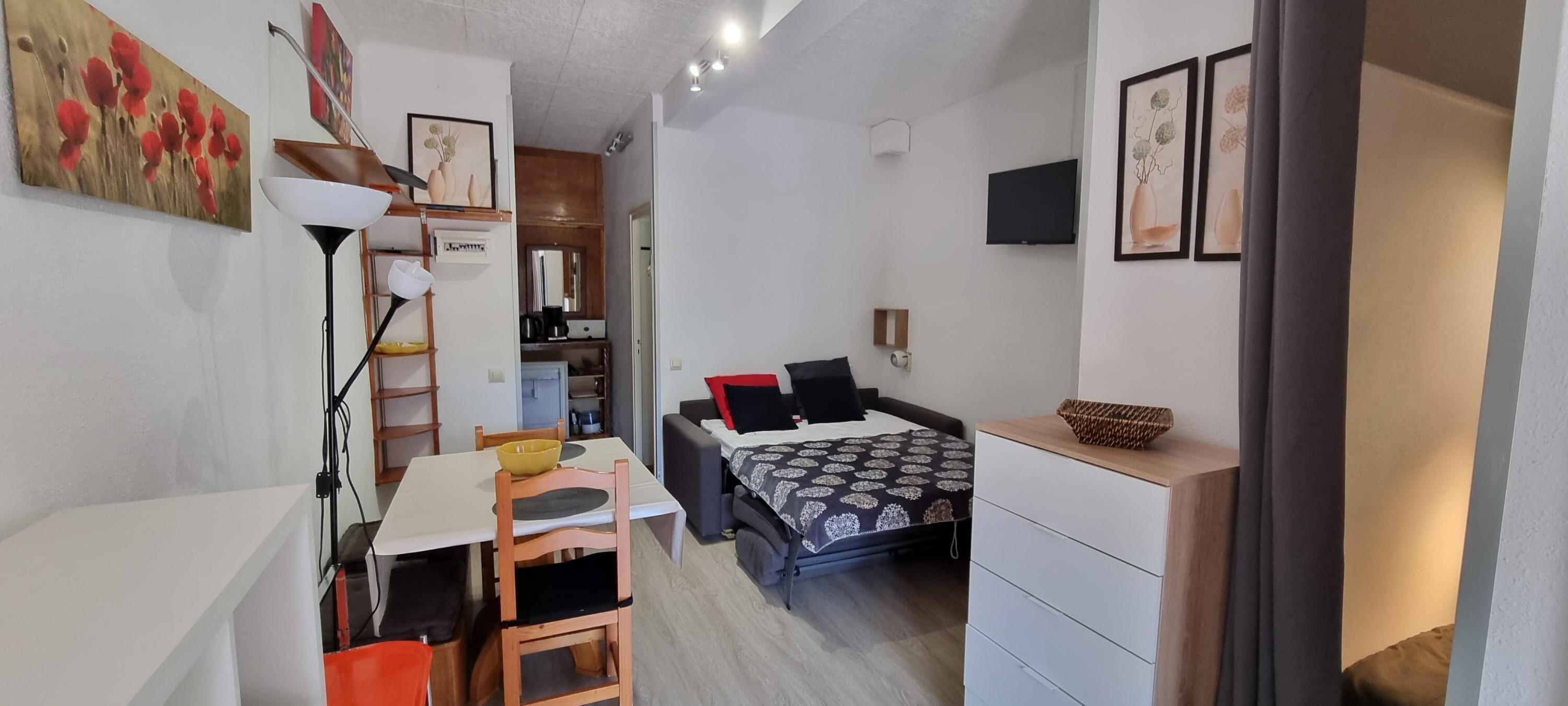 Un espacio habitable compacto con comedor, cama con ropa de cama estampada, televisor y obras de arte en las paredes.
