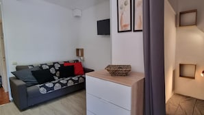 A modern living room with a sofa, a small white cabinet, a decorative bowl, and a wall-mounted TV. - TRES ESTRELLES CLUB 3-estudi 3 pers-Pas de la casa- 20 m piste-005986 (PAS DE LA CASA)