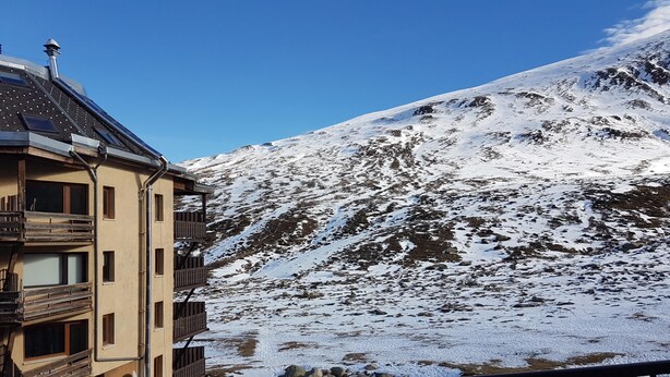 A multi-story building with balconies, a snow-covered mountain in the background, and a clear sky. - TRES ESTRELLES CLUB 3-estudi 3 pers-Pas de la casa- 20 m piste-005986 (PAS DE LA CASA)