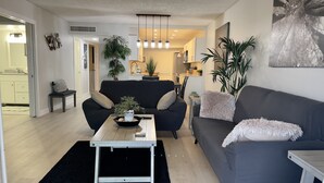 Een moderne woonkamer met een zwarte bank, een salontafel met een plant en een eethoek op de achtergrond.