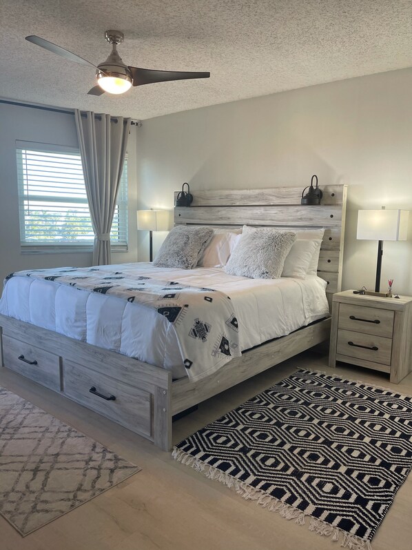 A bedroom with a bed, nightstands, a ceiling fan, and a window with curtains.