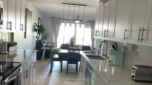 Een moderne keuken met witte kasten, een eethoek met tafel en stoelen, en een groot raam voor natuurlijk licht.