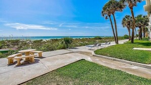 Een patio aan het strand met een betonnen tafel en banken, palmbomen en uitzicht op de oceaan.