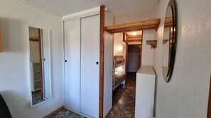 A narrow hallway with a wooden ceiling, a white door with a mirror, and a bunk bed in the background.