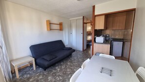 A compact living space with a sofa, a small table, and a kitchenette area.