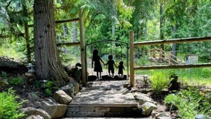 A stone pathway leading to a wooden structure with a metal gate, surrounded by lush greenery and trees. - Cabin With Hot Tub And Private Dock in Bottle Bay (Sagle)