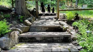 A stone pathway leading to a wooden structure with a metal gate, surrounded by lush greenery and trees.