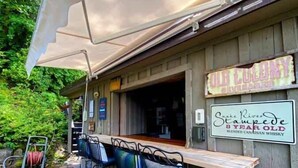 An outdoor bar area with a wooden table and chairs, a canopy, and signs advertising 'Old Colony' and 'Snake River Stampede 8 Year Old'. - Cabin With Hot Tub And Private Dock in Bottle Bay (Sagle)