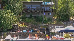 A lakeside cabin with a dock, outdoor seating, and a stone retaining wall. - Cabin With Hot Tub And Private Dock in Bottle Bay (Sagle)