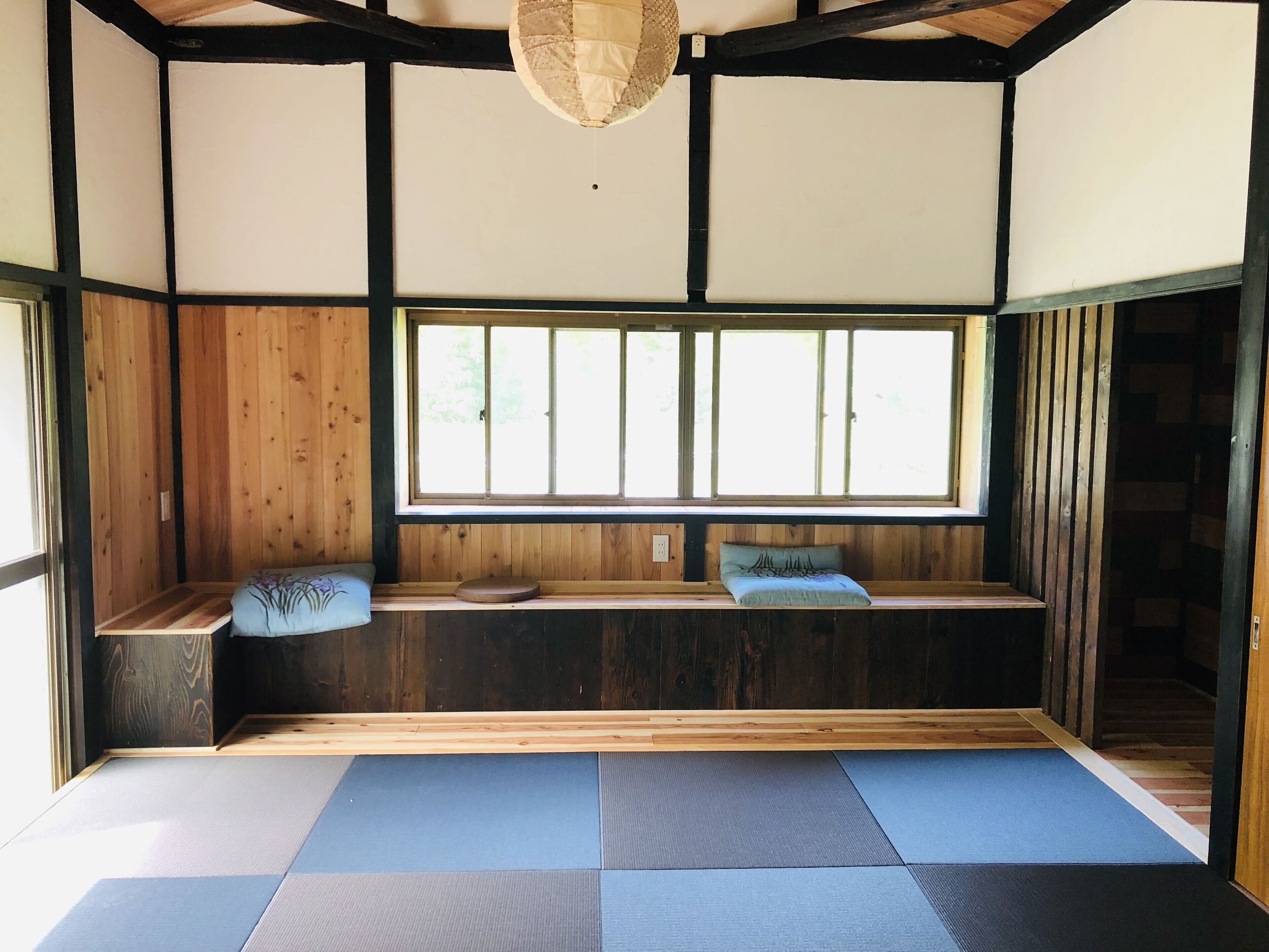 Une pièce de style japonais traditionnel, avec des tatamis, un banc en bois doté de coussins et une grande fenêtre.