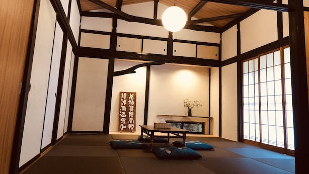 Une pièce de style japonais traditionnel, avec un sol recouvert de tatamis, une petite table basse entourée de coussins et un luminaire suspendu.
