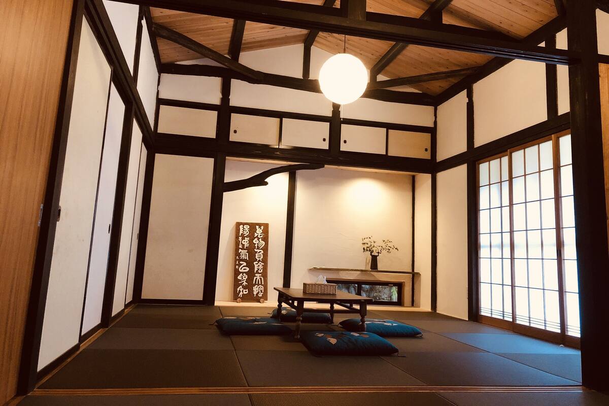 Une pièce de style japonais traditionnel, avec un sol recouvert de tatamis, une petite table basse entourée de coussins et un luminaire suspendu.