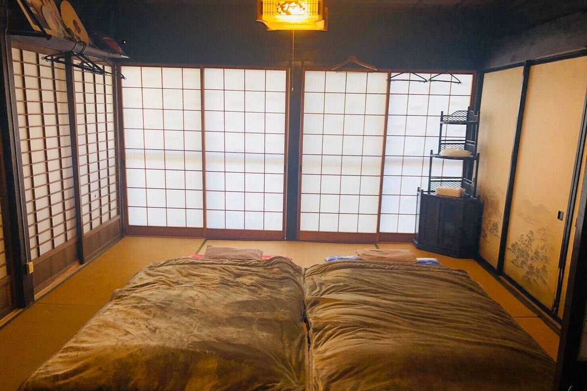 Une pièce traditionnelle japonaise avec un sol recouvert de tatamis, un futon servant de lit, des portes coulissantes en papier de riz (shoji) et une lanterne suspendue.