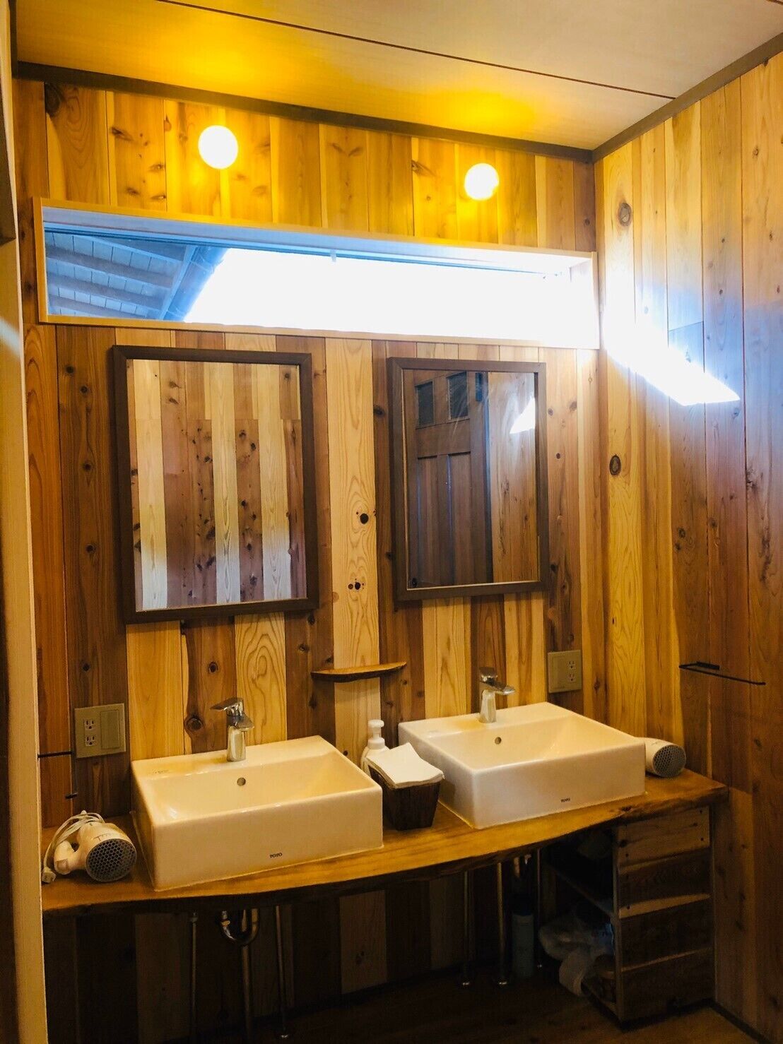 A wooden-paneled bathroom with two sinks, a mirror, and a shelf.