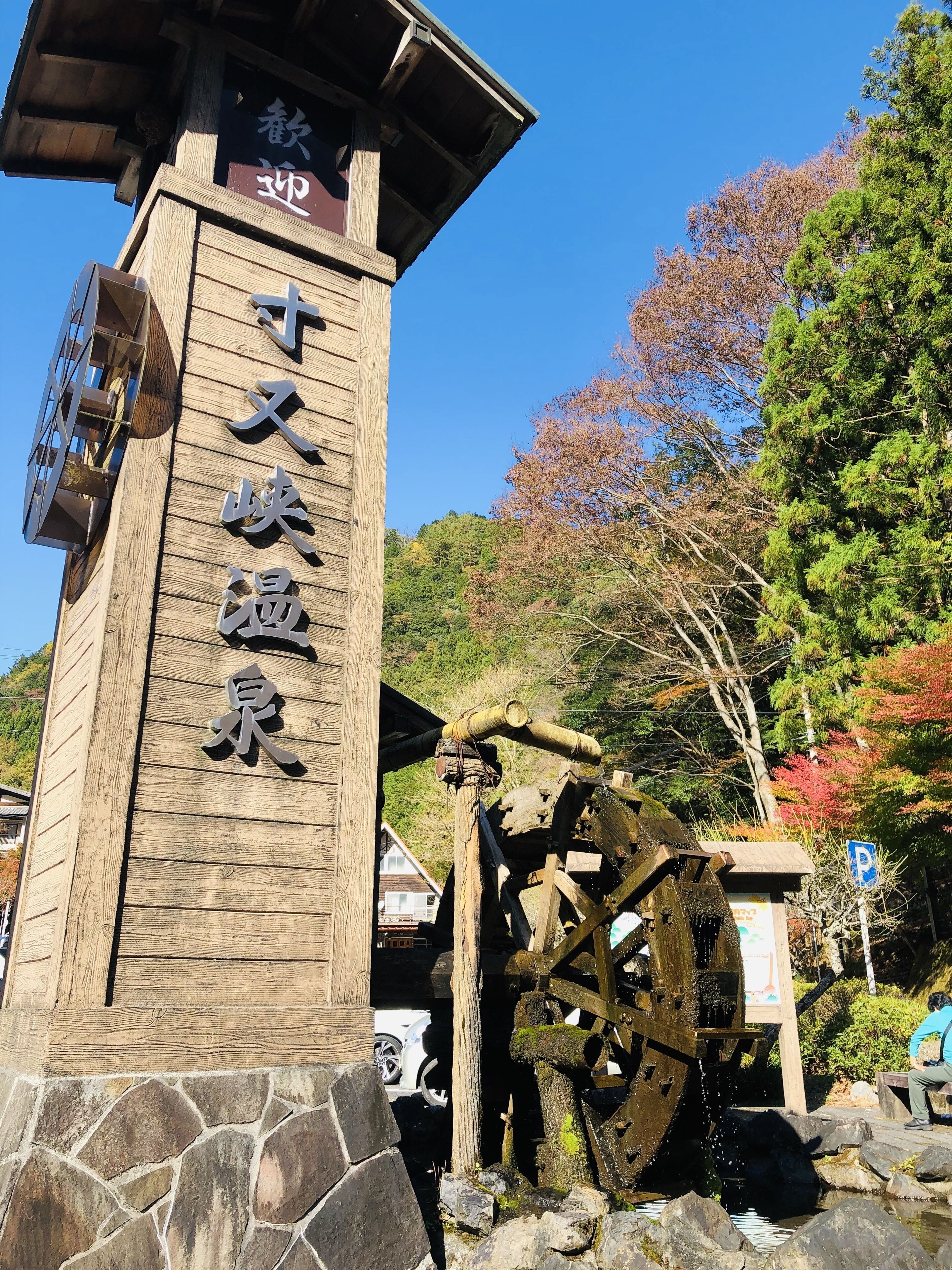 A wooden sign with Japanese characters, a traditional water wheel, and a stone pathway.