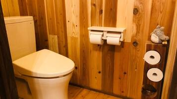 Bagno con rivestimenti in legno, un water, due rotoli di carta igienica e un piccolo ripiano con un peluche.