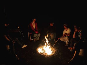 Un grupo de personas sentadas alrededor de una fogata en un entorno natural oscuro.