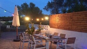 Une terrasse extérieure avec une table et des chaises en bois, des guirlandes lumineuses et des plantes en pot.