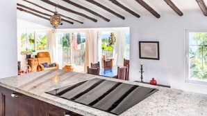 A modern kitchen with a large island, exposed wooden beams, and a view into a bright living area with a dining set.