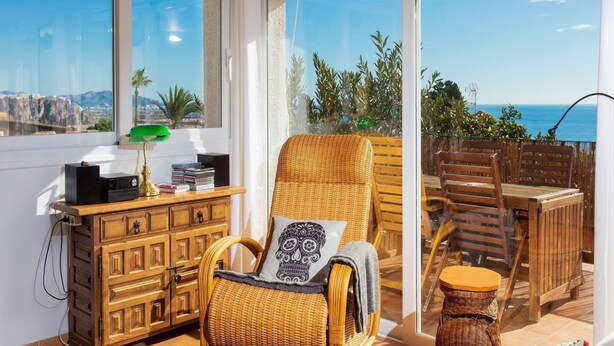 A balcony with wicker furniture, a wooden cabinet, and a view of the sea.