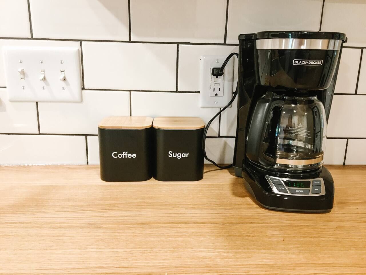 A coffee maker with two containers labeled "Coffee" and "Sugar" on a kitchen counter.