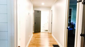 Un couloir doté d’un plancher en bois, de murs blancs et d’une porte donnant sur une pièce.