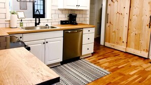 Une cuisine avec des meubles blancs, un lave-vaisselle, une machine à café et un plancher en bois.