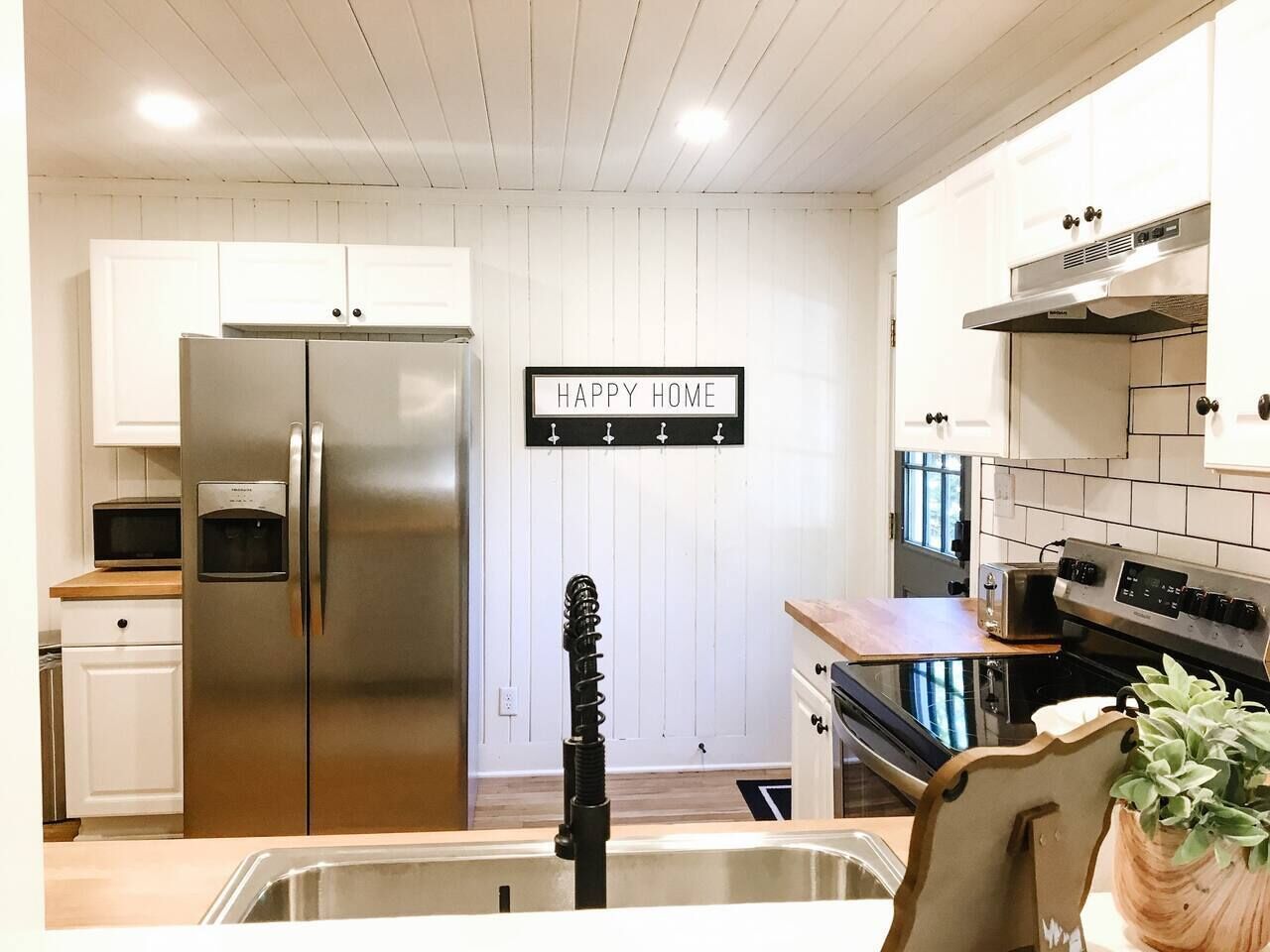 Een moderne keuken met roestvrijstalen apparatuur, een spoelbak en een bordje met de tekst 'HAPPY HOME'.